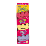 Packaged Scrub Mommy three-pack showing smiling face sponges in pink, yellow, and purple with product branding