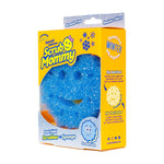 Close-up of Scrub Mommy yellow retail box showing a blue snowflake-shaped scrubber visible through a window and product text on the front.