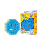 Blue Scrub Mommy snowflake-shaped scrubber sponge next to its yellow Scrub Mommy retail box with snowflake graphics.