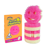 Scrub Mommy orange box next to a stack of pink-and-cream striped smiling scrub sponges on a white background