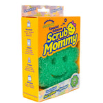 Green flower-shaped Scrub Mommy visible through an orange cardboard retail box showing branding and product window