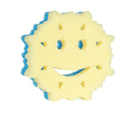 Face-on view of the yellow sponge side of a snowflake-shaped Scrub Mommy with smile and eye cutouts and blue abrasive layer visible on the edge.
