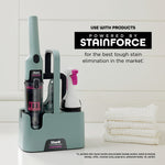 Shark StainForce portable cleaner and spray head displayed in a charging or storage caddy with stacked towels and branding panel.