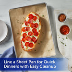 Sheet pan lined with unbleached parchment paper holding a pepperoni-topped open sandwich on a marble surface