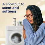 Person hugging a sweater in front of a blurred washer with text 'A shortcut to scent and softness' and a Downy bottle in background.