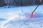 Action shot of an orange roller snow shovel pushing snow on a cleared walkway, handle extended into frame