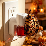 Side view of tortoiseshell pumpkin plug-in warmer attached to a wall outlet with seasonal tabletop decor blurred in background