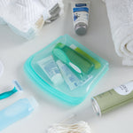 Teal silicone travel-sized storage bag holding toiletries displayed on a countertop with towels and personal care items