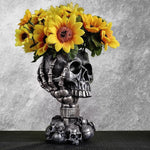Silver skull goblet planter filled with bright yellow sunflowers against a textured gray backdrop