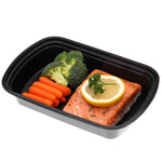 Close-up of a black single-compartment meal container holding salmon, baby carrots and broccoli on white background.