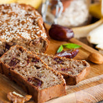 Sliced nut-and-date quick bread on a wooden cutting board with whole dates and almonds in soft focus