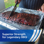 Person slicing a seasoned rack of ribs on a sheet of Reynolds Wrap aluminum foil outdoors