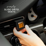 Hand sliding a Maison & Muse black square vent clip with amber insert onto a car vent