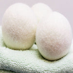 Close-up of three white wool dryer balls resting on a soft green towel
