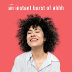 Smiling person with curly hair against a coral background with copy reading ‘an instant burst of ahhh’