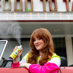 Woman in a convertible smiling while spraying a Citrus Magic Limoncello car spray with visible mist