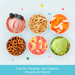 Overhead view of six paper snack cups filled with ice cream, pretzels, candy and snacks against a pale background