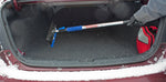 Telescoping snow broom with foam grip stored inside a car trunk next to a red travel bag