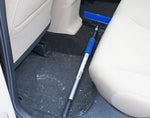 Snow broom with blue bristles and foam handle placed on a vehicle floorboard beside a seat