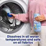 Hand holding a blue measuring cup pouring Snuggle scent booster granules into a front-load washer while holding the product bottle.