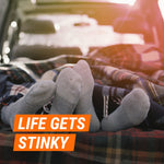Pair of sock-covered feet on a blanket in a car trunk with overlay text ‘Life Gets Stinky’ suggesting odor issues