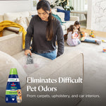 Person cleaning a sofa cushion with a portable cleaner while children play in the background and BISSELL spot-and-stain bottle inset.