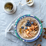 Styled overhead shot of a SOLO patterned paper bowl containing oatmeal topped with fruit and nuts on a napkin