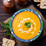 Styled top view of a SOLO patterned paper bowl filled with creamy orange soup and a parsley garnish