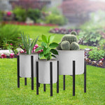 Three black metal plant stands of varying heights displayed outdoors holding white planters