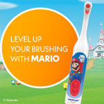 Close-up of a Super Mario Spinbrush electric toothbrush on a grassy Nintendo-style background with text bubble reading 'Level up your brushing with Mario'.