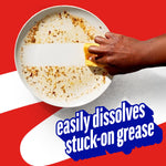 Hand using a sponge to clean a heavily soiled plate with text claiming it ‘easily dissolves stuck-on grease’