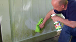 Person using a trigger bottle of Spray Nine to clean a stained outdoor fence panel, wiping with a green cloth.