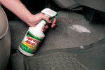 Hand holding a Spray Nine bottle aimed at a car floor carpet with visible cleaning foam or residue
