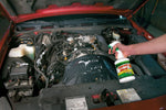 Hand holding and spraying a Spray Nine bottle over a car engine bay with the vehicle hood open