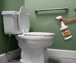 Person spraying Spray Nine cleaner toward a toilet bowl in a small bathroom with green walls and grab bar