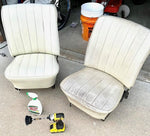 Two white vinyl car seats on a garage floor with a Spray Nine bottle and drill brush placed nearby