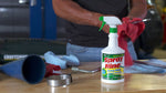 Workshop countertop scene featuring a Spray Nine trigger spray bottle in front of tools and shop rags, person working in background.