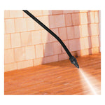 Sprayer wand tip emitting a fine spray over a wooden deck beside a shingled wall, lifestyle cleaning shot.