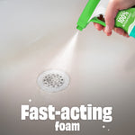 Close-up of a hand spraying fine white foam from a Scrubbing Bubbles trigger bottle onto a bathtub drain