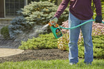 Person spraying an Ortho WeedClear bottle attached to a hose, water spraying over lawn and plants