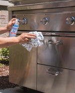 Person spraying and wiping a stainless steel outdoor grill with a Sprayway stainless steel cleaner can and cloth