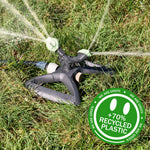 Rotating lawn sprinkler in grass actively spraying water, with a green circular badge reading +70% recycled plastic.