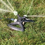 Rotating garden sprinkler in grass spraying multiple water streams, triangular base and mint spray heads visible.