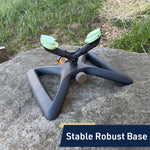 Mint and black rotating sprinkler placed on a rock outdoors, close-up showing the stable triangular base and adjustable spray heads.