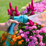 Close-up of a hand squeezing a teal Sprout nozzle producing a flat spray over colorful garden flowers