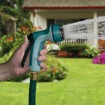 Hand holding teal Sprout rear-trigger nozzle spraying a strong jet with a house and lawn blurred in background