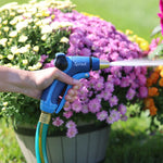 Side view of a person holding a blue Sprout hose nozzle spraying a steady stream toward flowering plants.