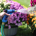 Blue Sprout adjustable nozzle in hand producing a wide spray over vibrant potted flowers outdoors.