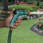 Hand holding a Sprout front-trigger nozzle firing a solid water stream with a landscaped garden background