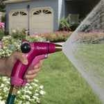 Hand holding a pink Sprout garden nozzle connected to a hose, spraying a wide stream in a yard